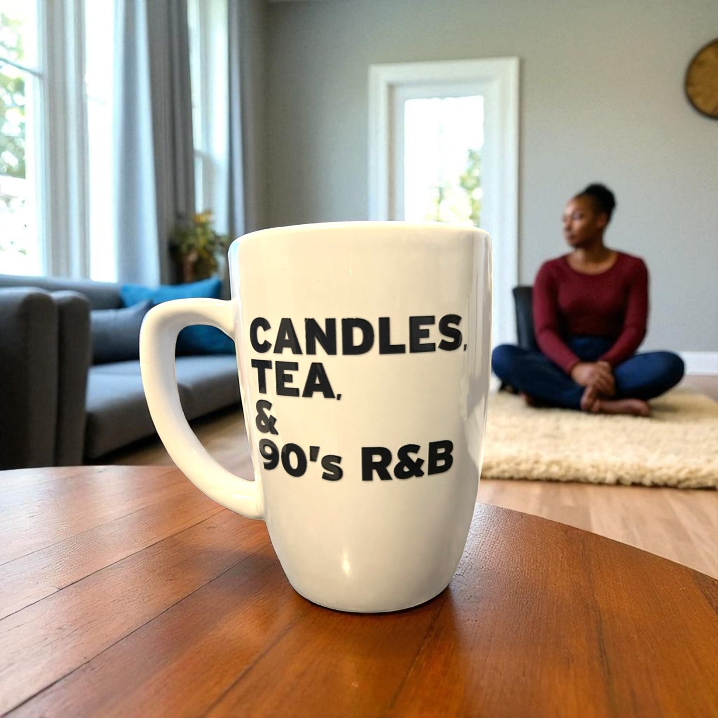 White mug with text on a wooden table in a living room with a person sitting in the background.