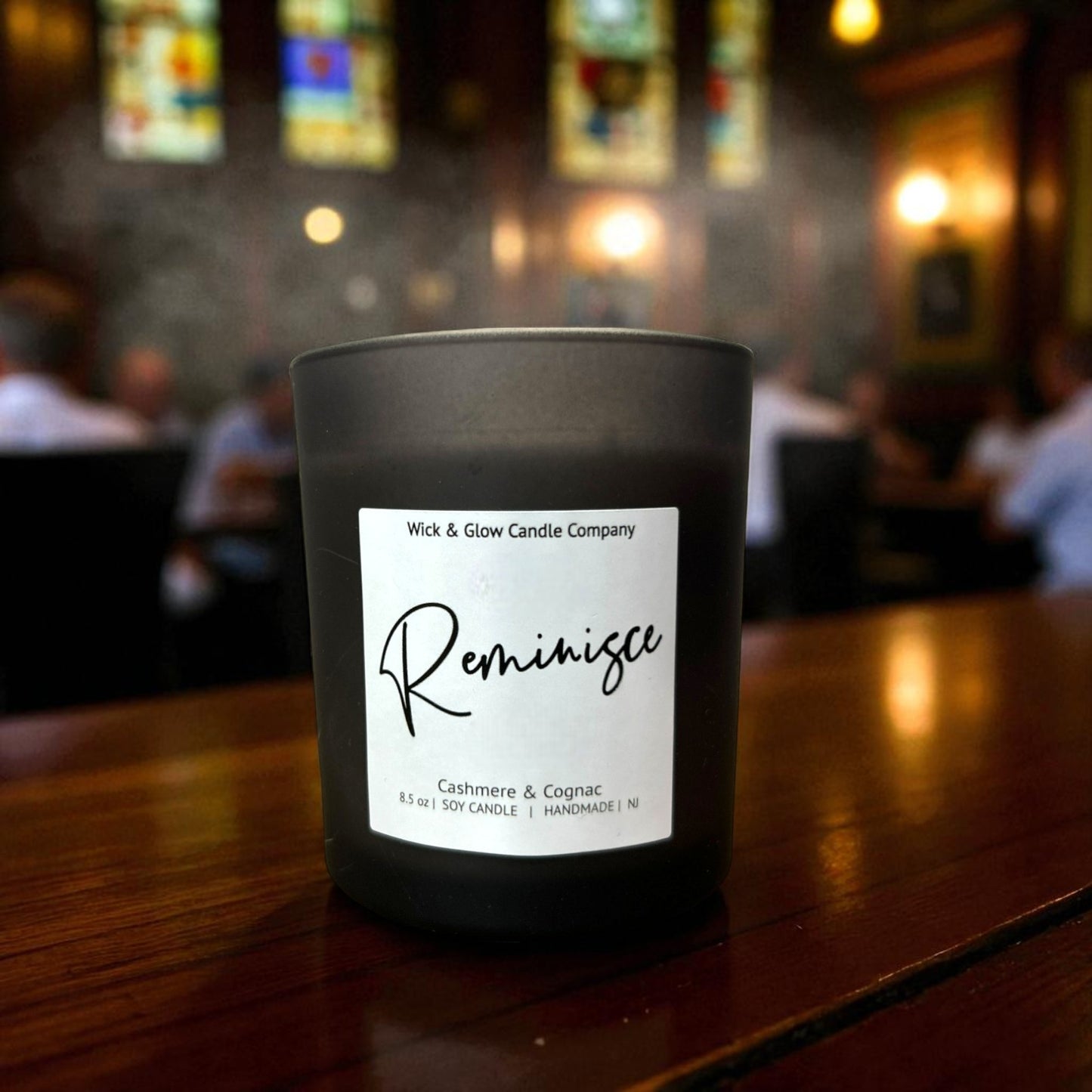 Candle labeled 'Reminisce' by Wick & Glow Candle Company on a wooden surface with a blurred background