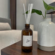 Brown diffuser bottle with white sticks on a wooden table next to a white vase.