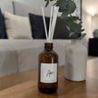 Aromatherapy diffuser bottle labeled 'Adore' on a wooden surface with a blurred living room background.