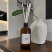 Brown diffuser bottle with white sticks and a label on a wooden surface.