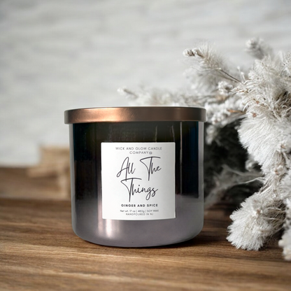 Wick and Glow's luxury soy wax candle in a gray glass container on a wooden table  with a white branch. The sent is Ginger and spice