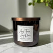 Candle with a label on a marble surface, with a plant in the background