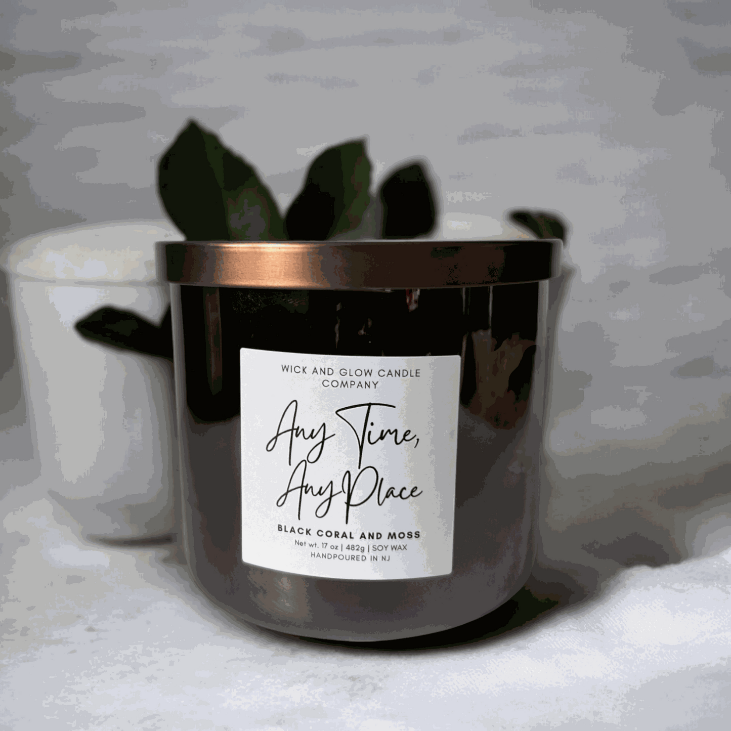 Wick and Glow's large luxury soy wax candle in a gray glass container on a white table with a plant