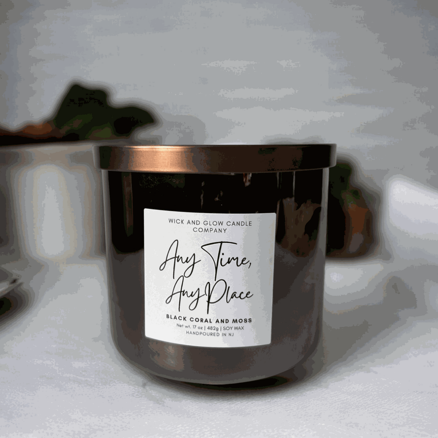 Wick and Glow's large luxury soy wax candle in a gray glass container on a white table with a plant