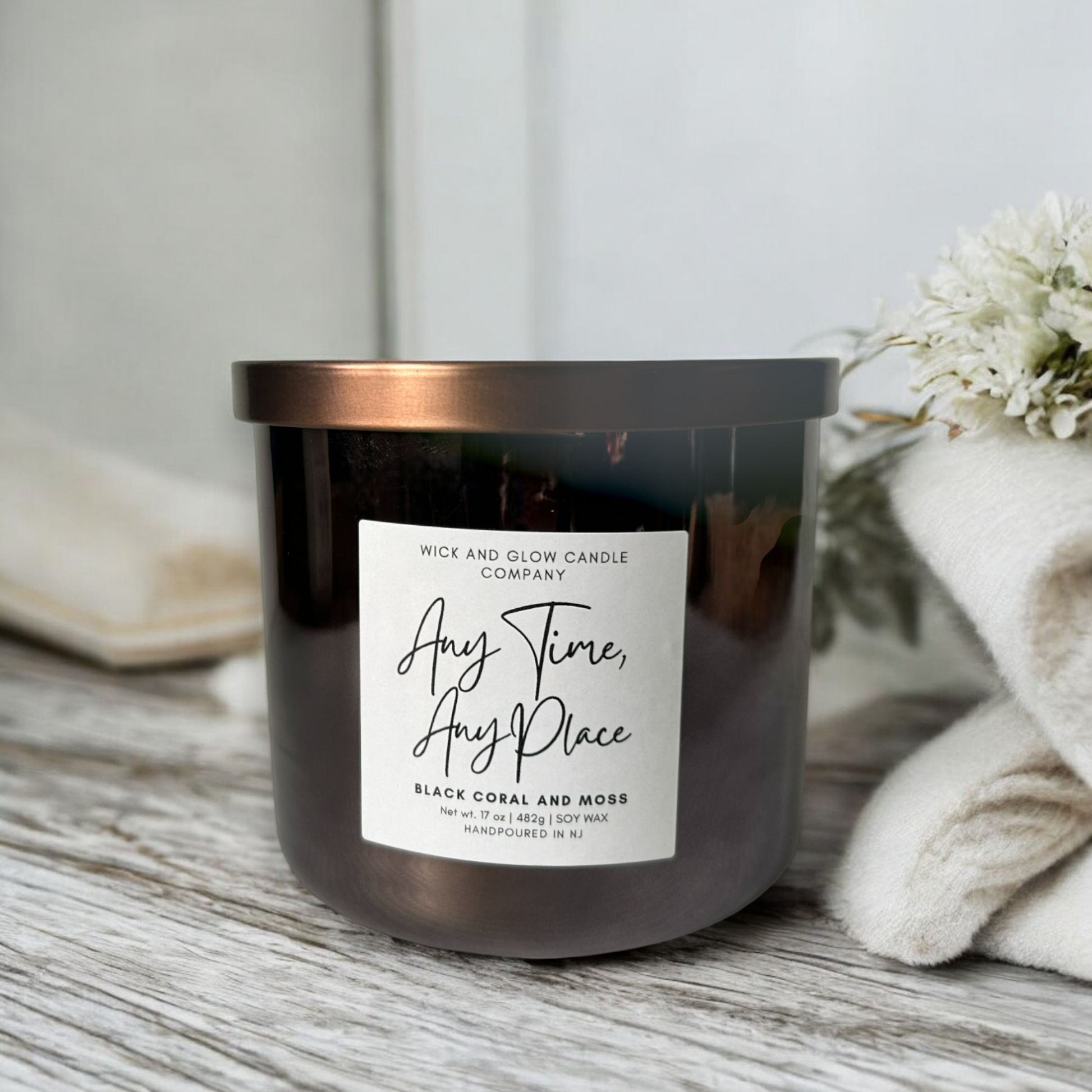 Large candle in a silver jar with a bronze lid on a gray grain table. The scent is Black Coral and Moss.