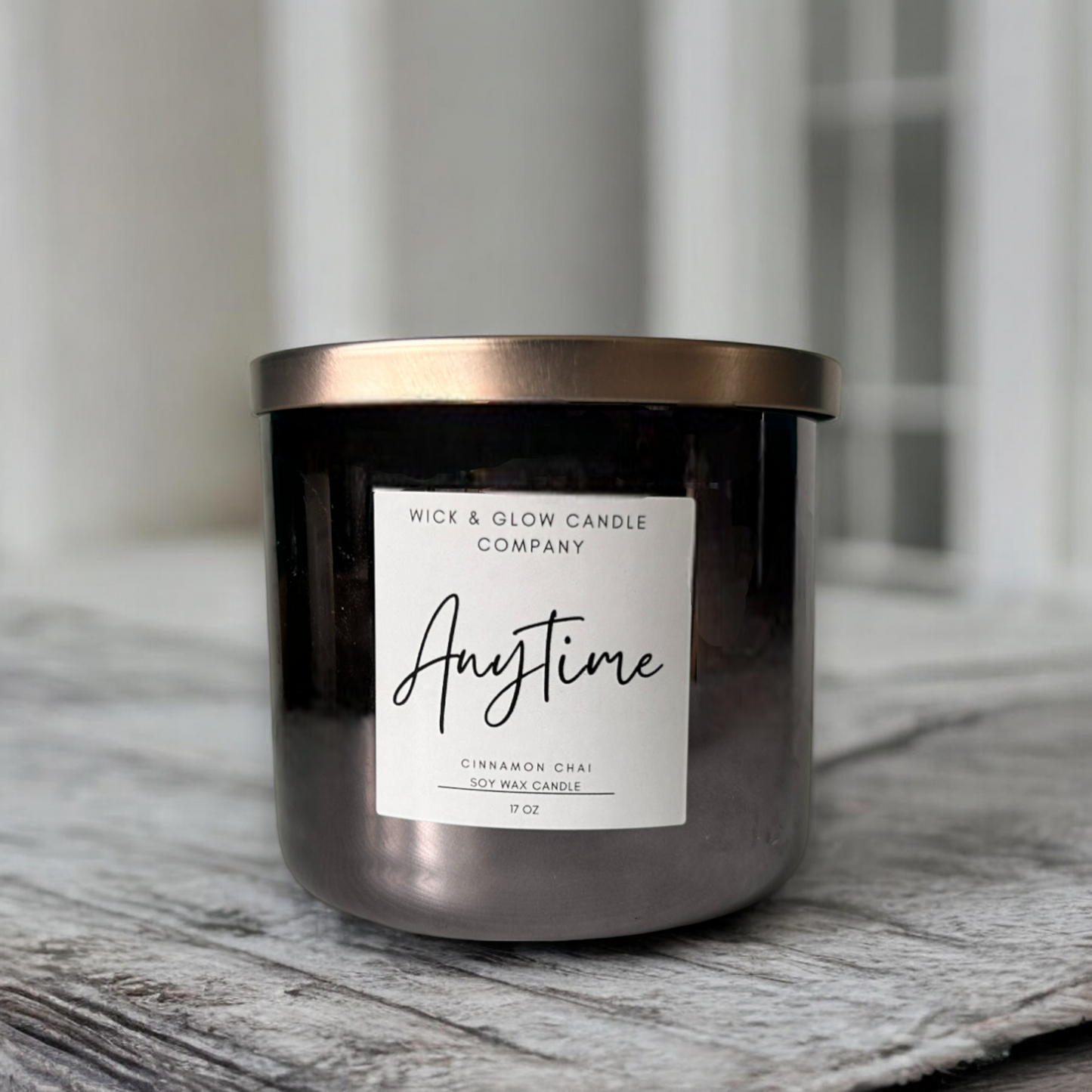 Wick and Glow's luxury soy wax candle in a gray jar with a bronze lid on a gray grain table