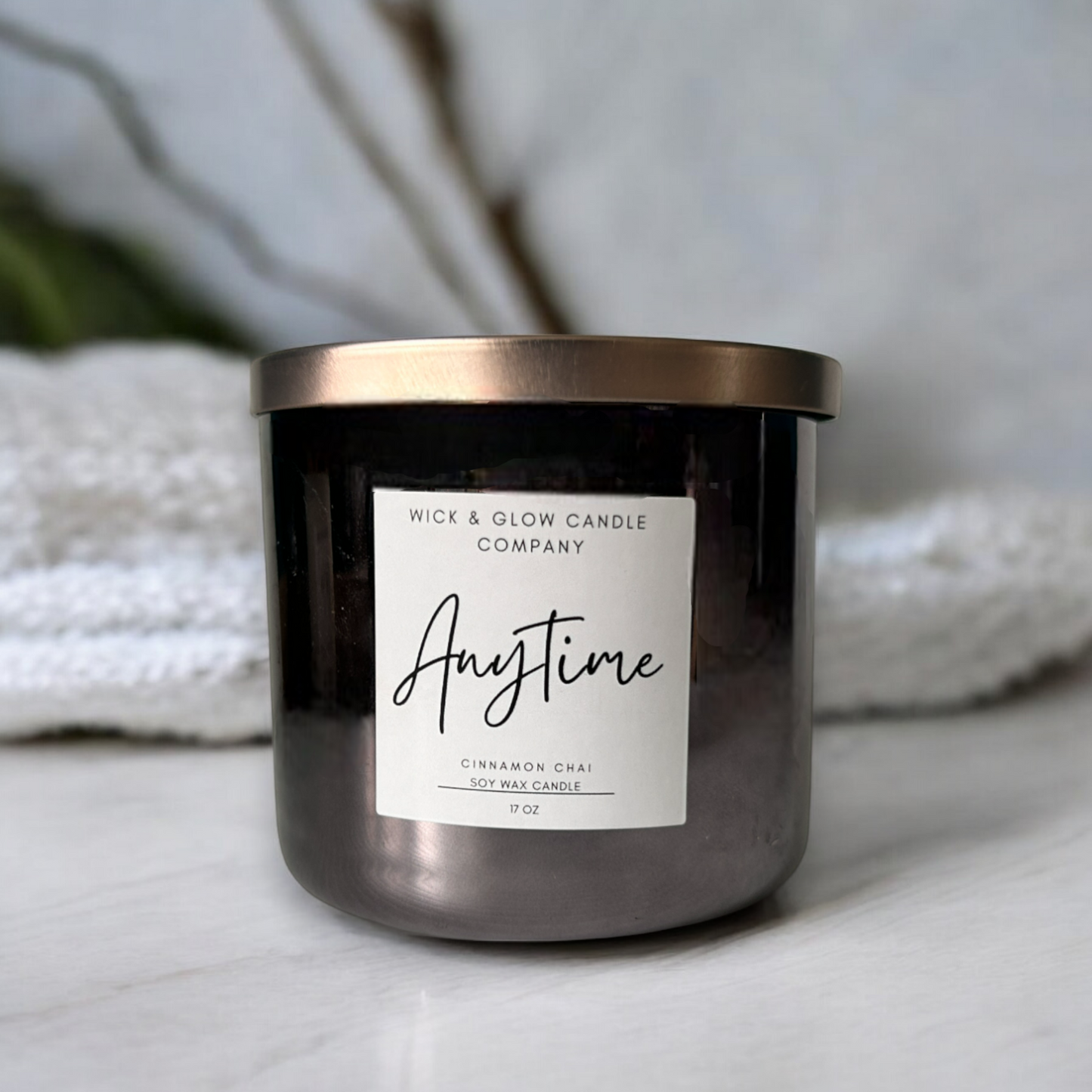 Wick and Glow's luxury soy wax candle in a gray jar with a bronze lid on a white marble table.