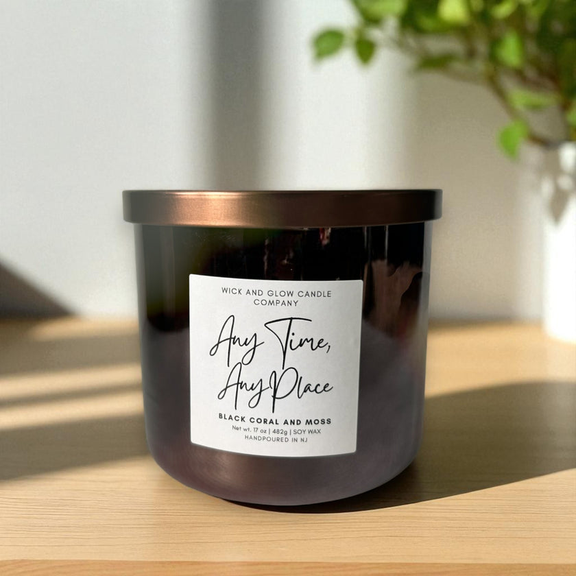 Candle with a label on a wooden surface, with a plant in the background