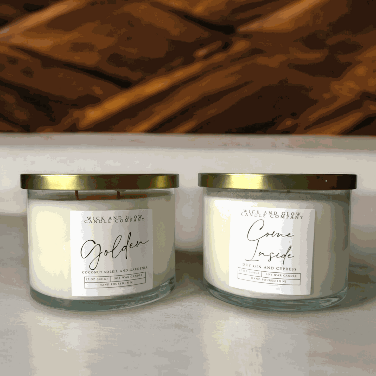 Wick and Glow's large luxury soy wax candles in a clear glass containers with a gold lid on a tan table with a wood background