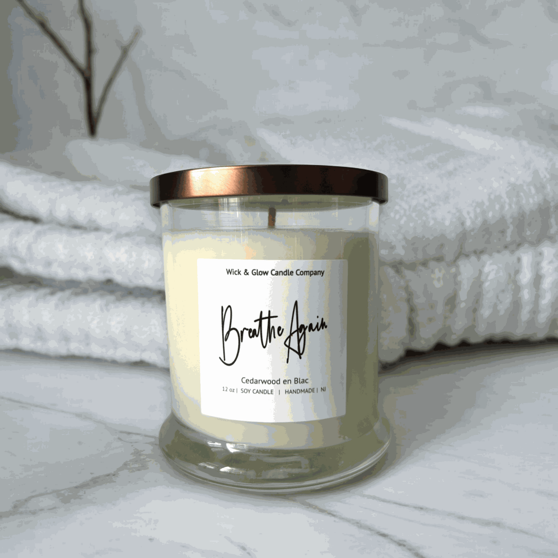 Wick and Glow's luxury soy wax candle in a clear glass container on a marble table with white flowers. The scent is Cedarwood.