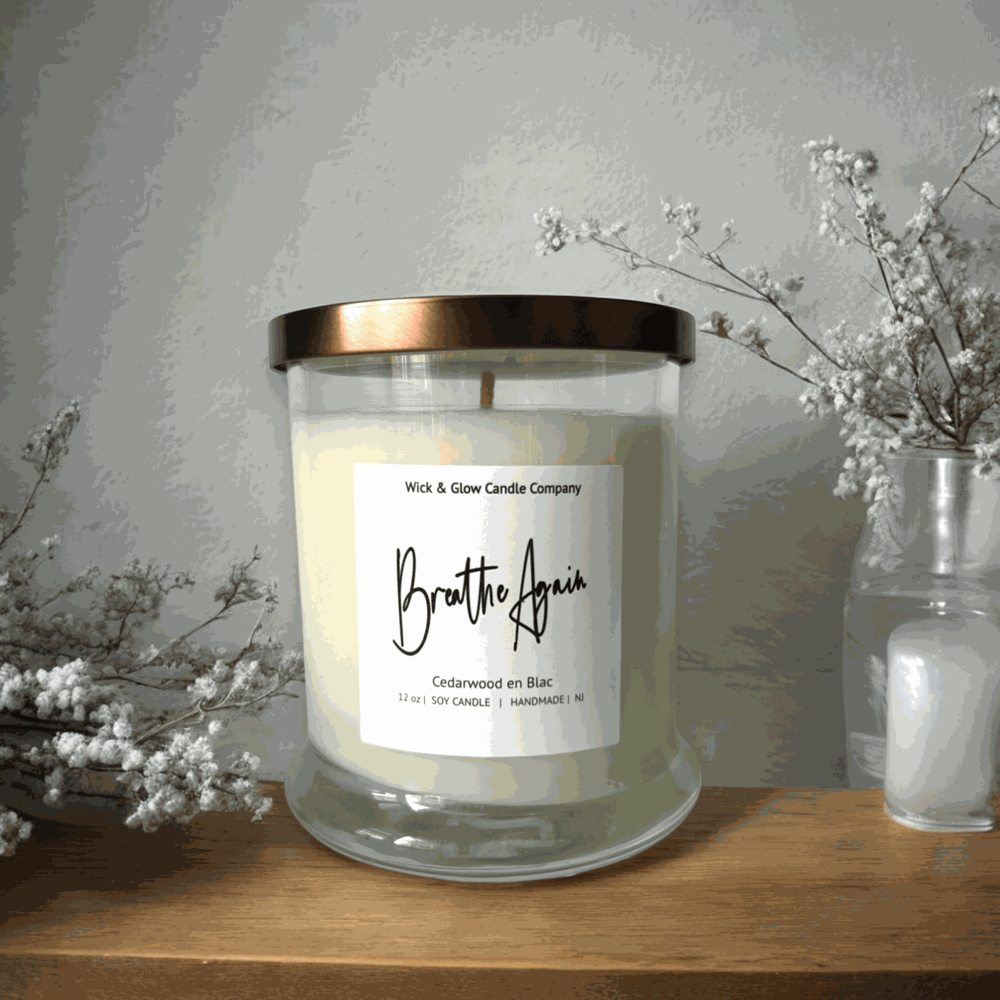 Wick and Glow's luxury soy wax candle in a clear glass container on a wooden table with white flowers. The scent is Cedarwood.