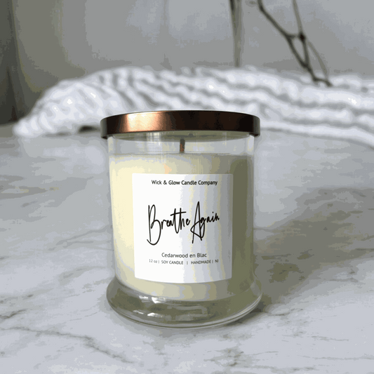 Wick and Glow's luxury soy wax candle in a clear glass container on a white marble table with white flowers. The scent is Cedarwood.