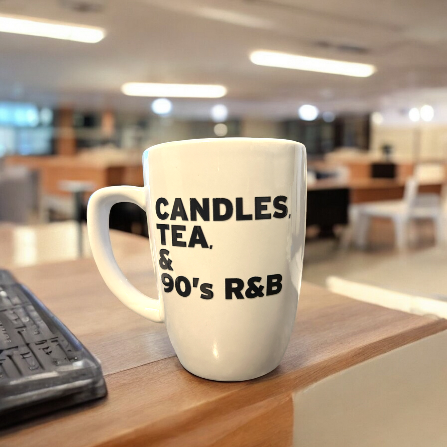 Candles, tea, and 90s R&B mug on desk in cozy setting.