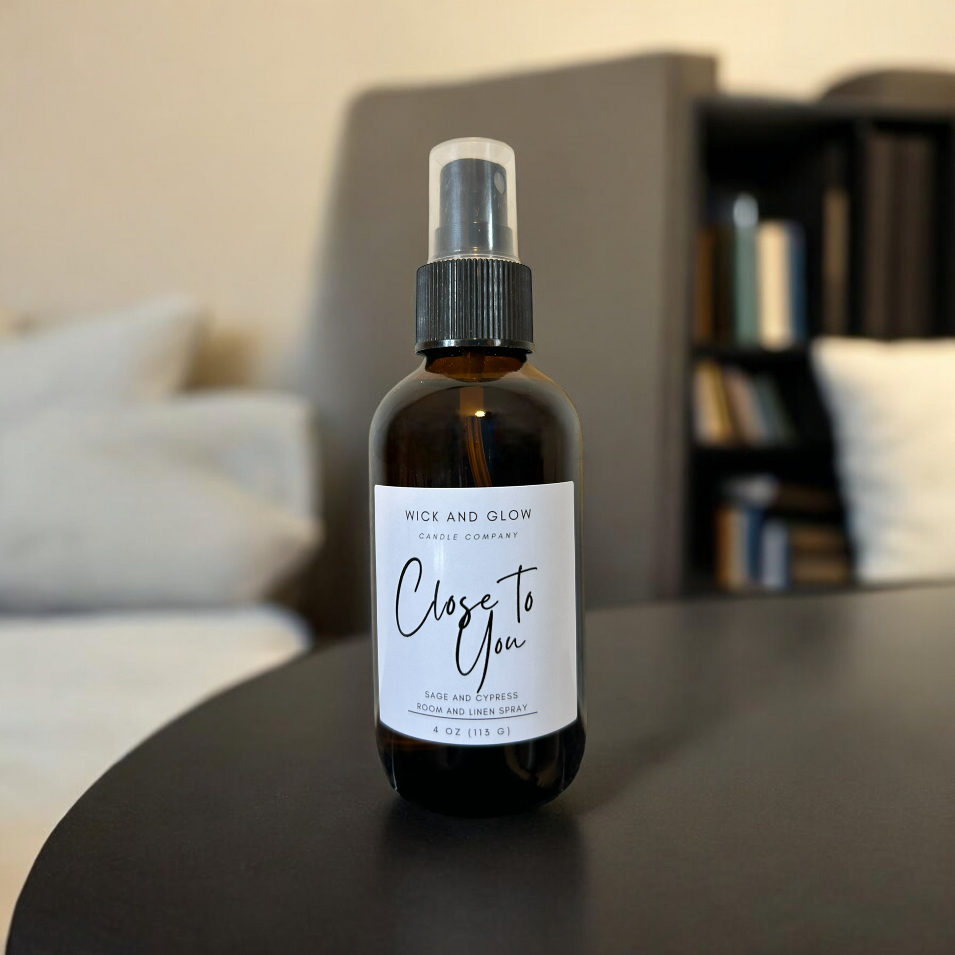 Amber spray bottle  with a white label from the Wick and Glow Candle Company on a black table with a white in the background ; the scent is sage and cypress.