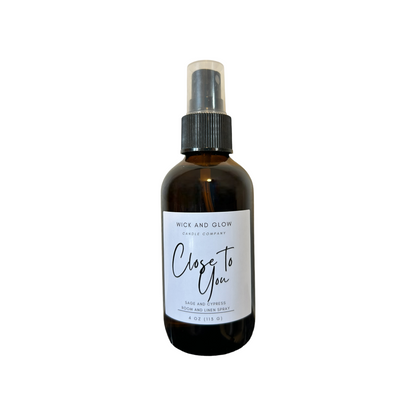 Amber spray bottle  with a white label from the Wick and Glow Candle Company on a with a white in the background ; the scent is sage and cypress.