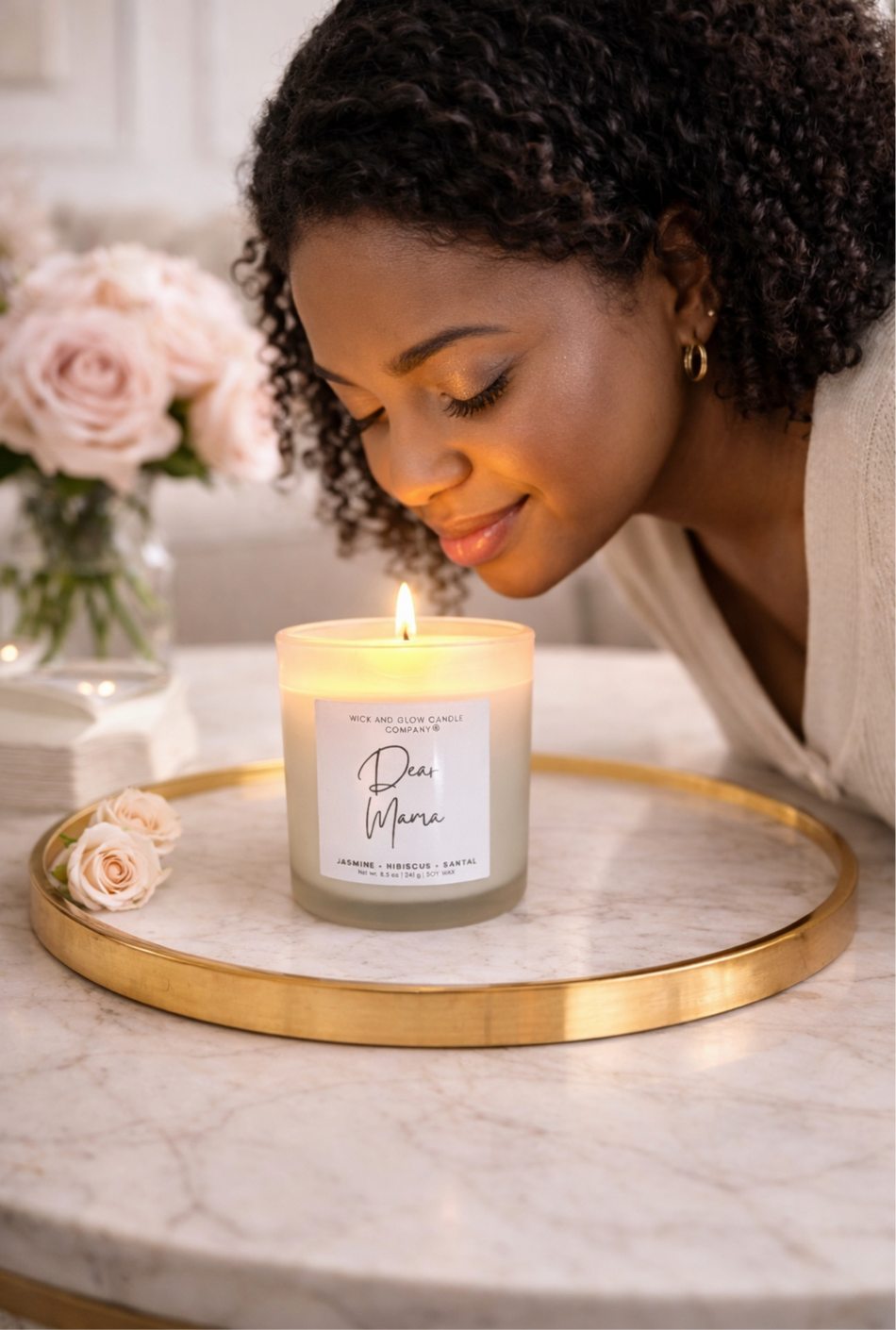 Woman smelling a candle on a marble surface with flowers in the background