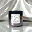 A dark metallic glass jar candle with a white label reading 'Diamonds & Pearls' and 'Rick and Glow Candle Company,' set against draped white satin fabric.