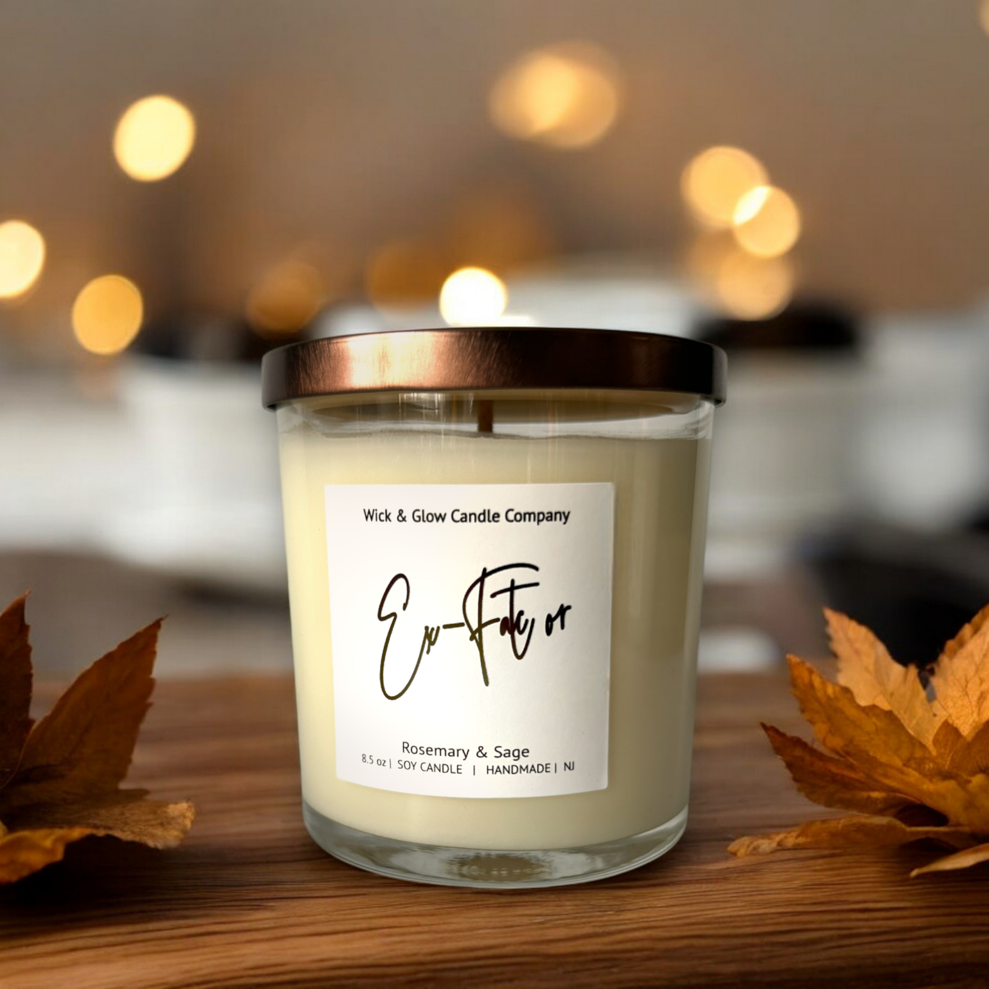 White candle in a clear jar with a bronze lid on a wooden table surrounded by leaves. The scent is rosemary and sage