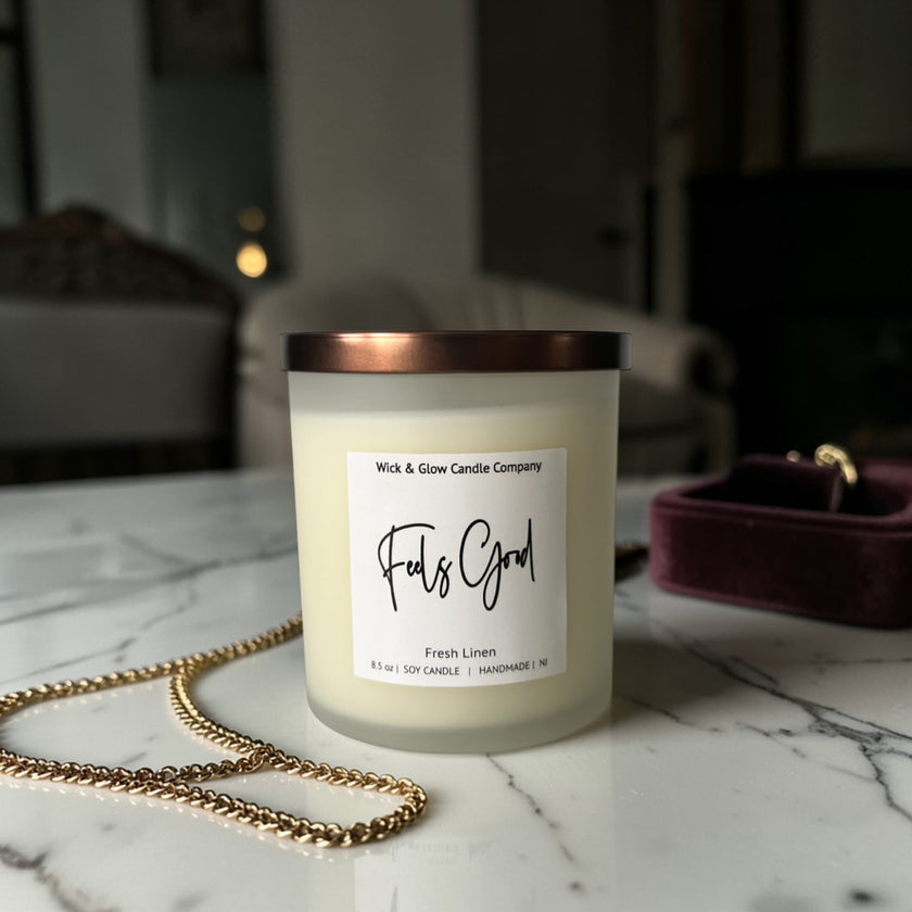 Candle labeled 'Feels Good' by Wick & Glow Candle Company on a marble surface with a blurred background.