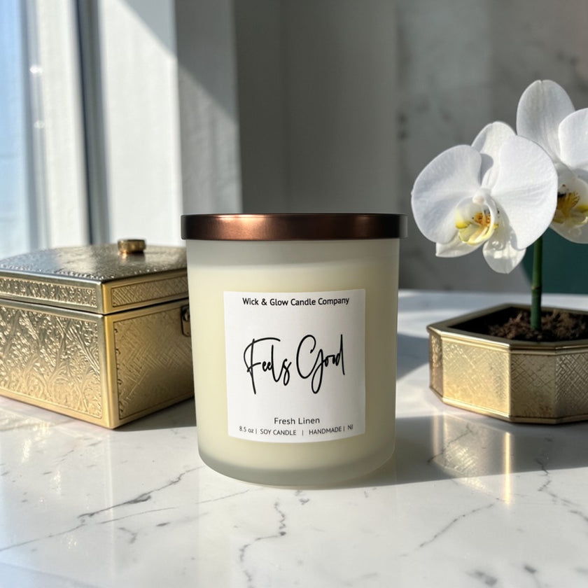 Candle labeled 'Feels Good' by Wick & Glow Candle Company on a marble surface with a decorative box and orchid.