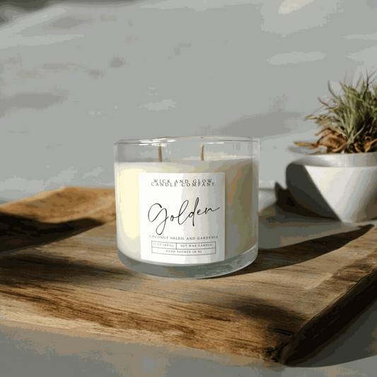 A white candle in a clear glass jar with a white label on a wooden table from Wick and Glow Candle Company