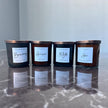 Four black candles with labels on a reflective surface by Wick and Glow
