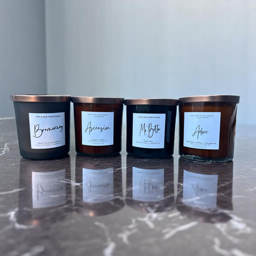 Four black candles with labels on a reflective surface by Wick and Glow