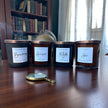Four candles with labels on a wooden surface, with a magnifying glass in front.