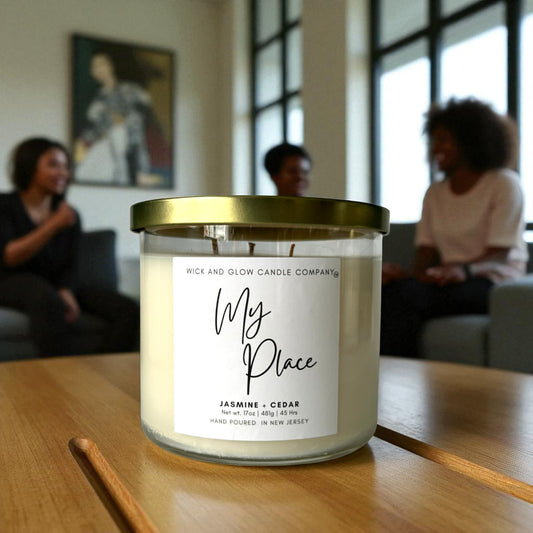 Candle labeled 'My Place' by Wick and Glow Candle Company on a wooden table with people in the background.