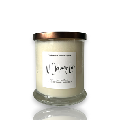 White candle in a clear jar with a bronze lid on a white background. The scent is spiced honey and tonka