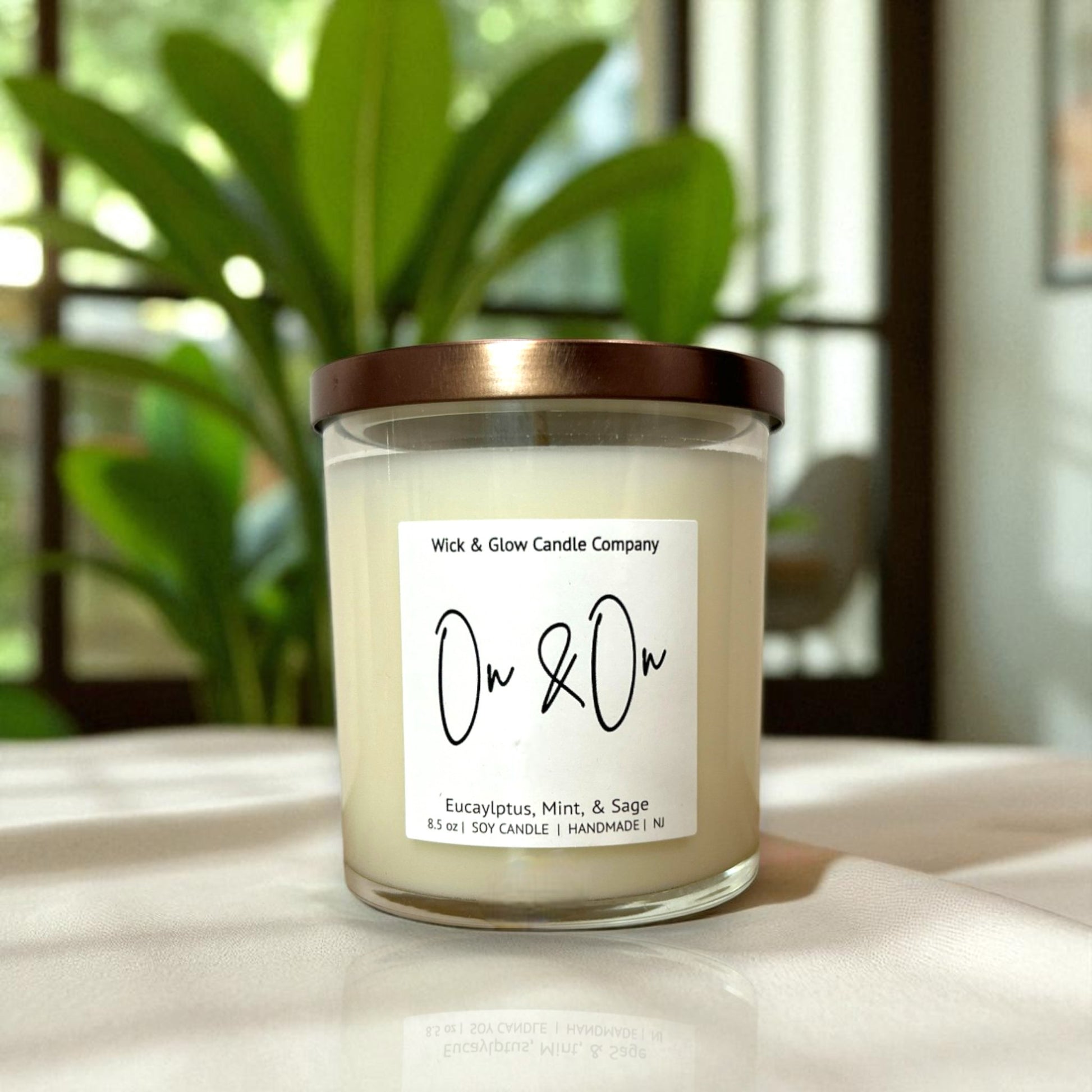 Candle with a label on a surface, featuring a plant in the background