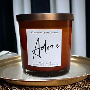 Candle in a brown jar with a bronze lid  on a gold tray and a label that read Adore