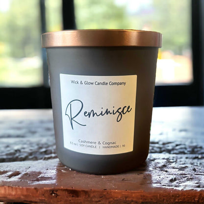 A brown glass jar candle with a label that reads 'Reminisce' and includes details about the candle's scent and wick material.