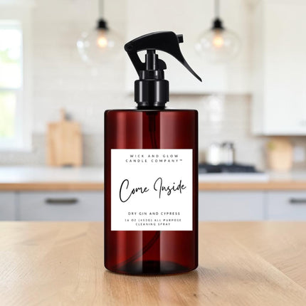 A dark amber spray bottle with a black trigger top and a white label reading 'Come Inside' by Mice and Glow Candle Company, placed on a wooden table with a softly blurred kitchen background.