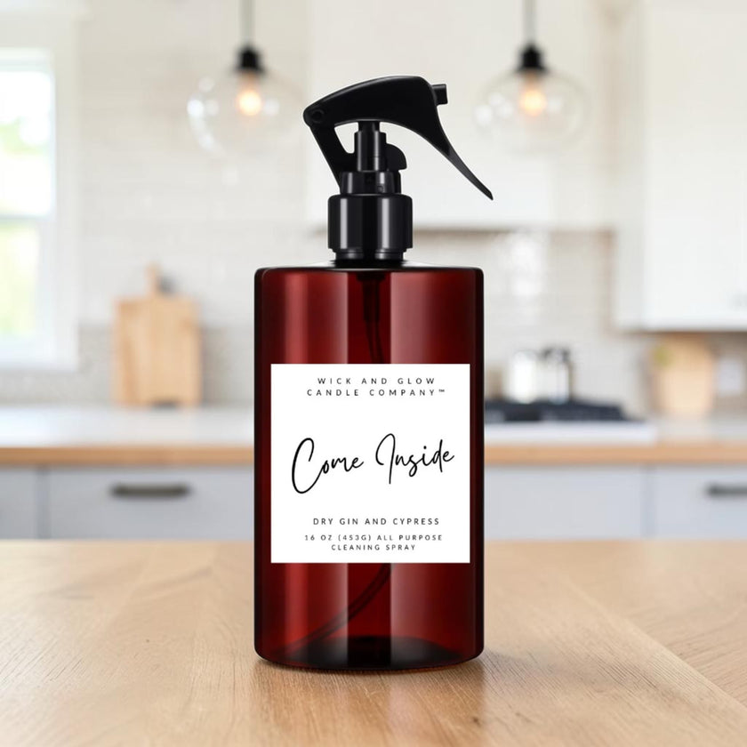 A dark amber spray bottle with a black trigger top and a white label reading 'Come Inside' by Mice and Glow Candle Company, placed on a wooden table with a softly blurred kitchen background.