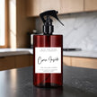 A dark amber glass spray bottle with a black trigger sprayer and a white label reading 'Come Inside' by Mice and Glow Candle Company, set on a dark countertop with a blurred kitchen background.