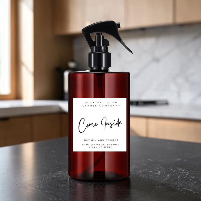 A dark amber glass spray bottle with a black trigger sprayer and a white label reading 'Come Inside' by Mice and Glow Candle Company, set on a dark countertop with a blurred kitchen background.