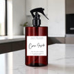 A dark amber glass spray bottle with a black trigger top and a white label reading 'Come Inside' by Mice and Glow Candle Company, set on a white marble countertop in a softly blurred kitchen background.