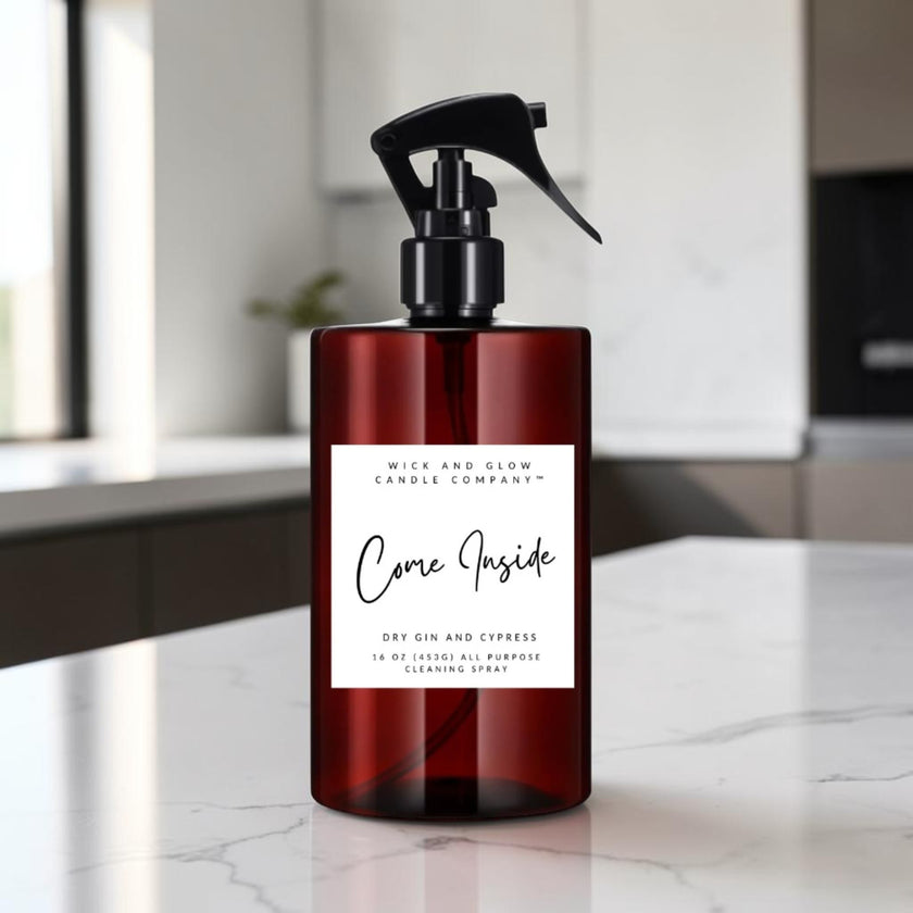A dark amber glass spray bottle with a black trigger top and a white label reading 'Come Inside' by Mice and Glow Candle Company, set on a white marble countertop in a softly blurred kitchen background.