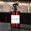 A dark amber glass cleaning spray bottle with a black trigger sprayer and a white label reading 'Come Inside' by Mice and Glow Candle Company, set on a dark countertop with a softly blurred kitchen background.