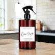 A dark amber glass spray bottle with a black trigger sprayer and a white label reading 'Come Inside' by Mice and Glow Candle Company, set on a wooden surface with a softly blurred kitchen background.