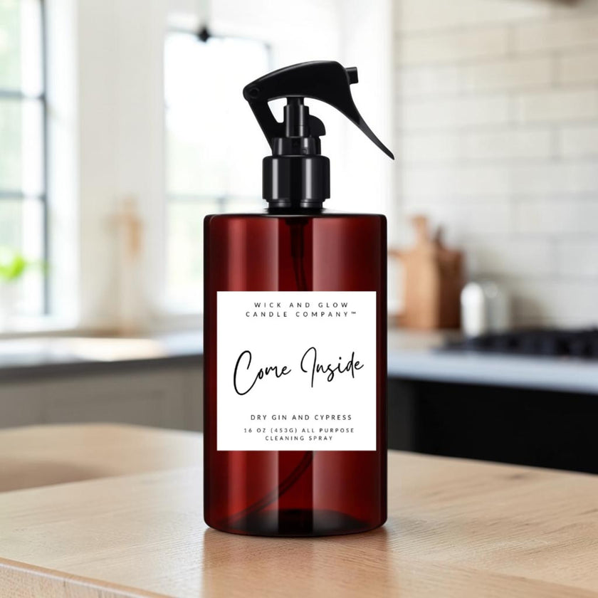 A dark amber glass spray bottle with a black trigger sprayer and a white label reading 'Come Inside' by Mice and Glow Candle Company, set on a wooden surface with a softly blurred kitchen background.