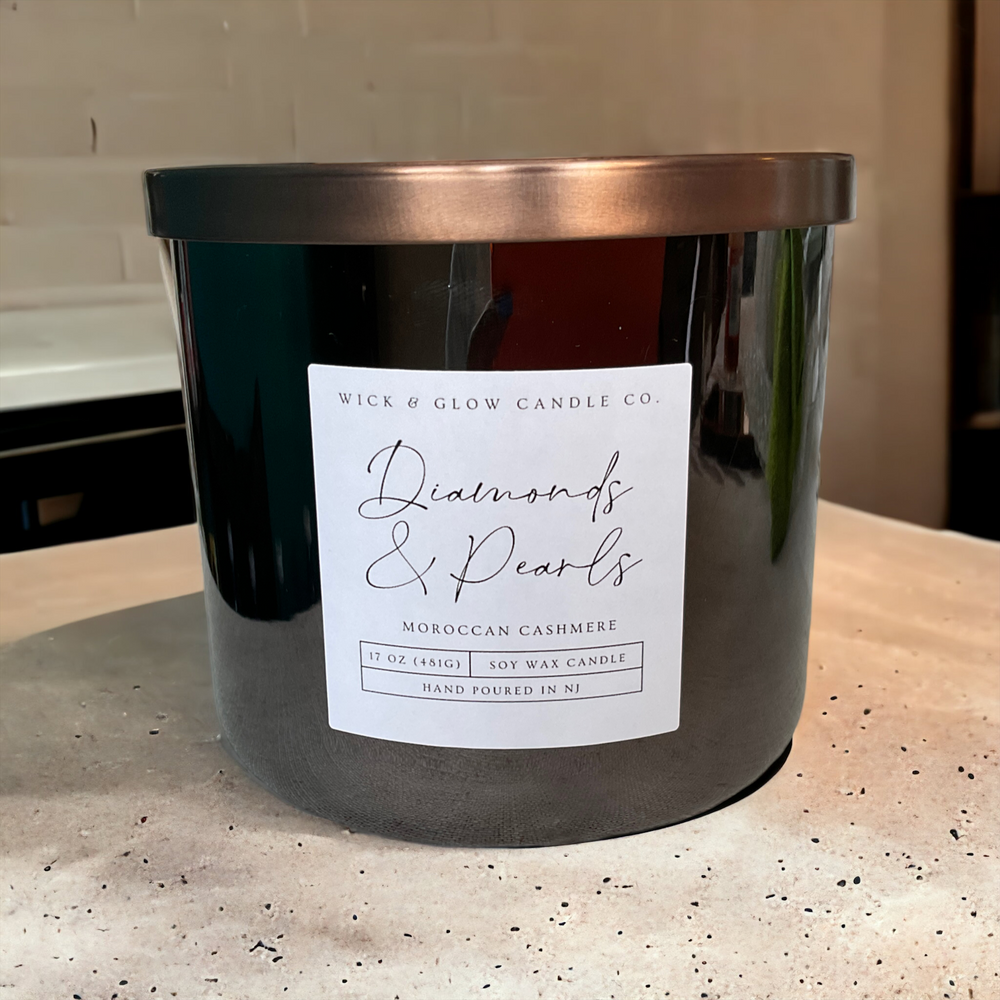 Grey candle with a bronze lid on a concrete countertop with a white label that reads Diamonds and Pearls
