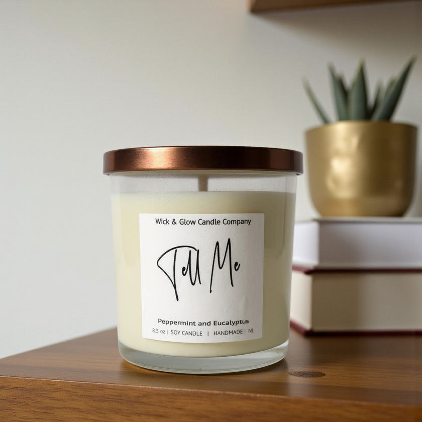 Candle with a label on a wooden surface, with a plant and books in the background